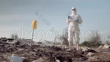 生态灾害，妇女穿着防护服，戴着口罩，在垃圾填埋场附近张贴有防止污染标语的海报